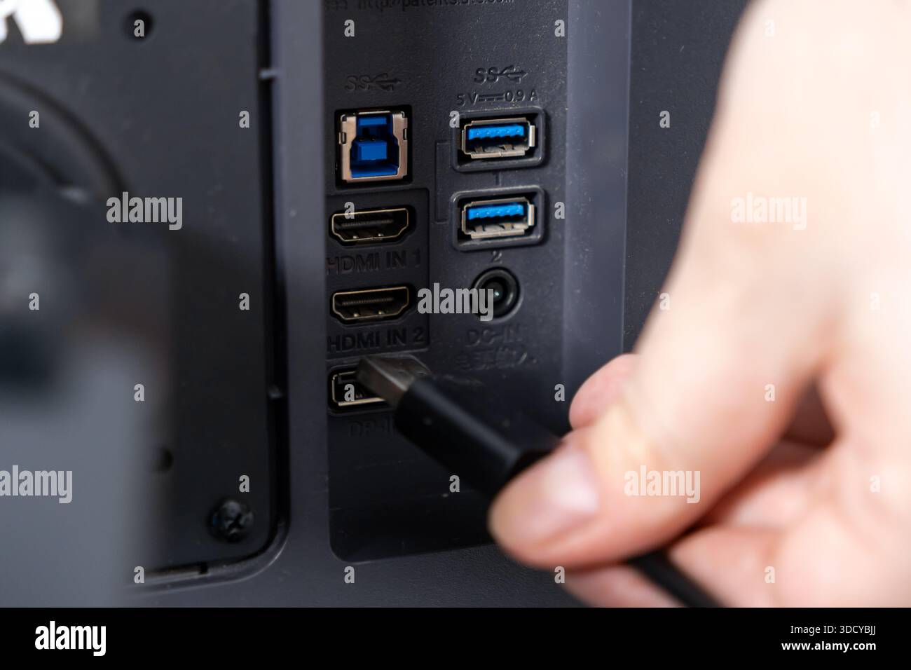 Top view of a hand connecting a black cable to a display device's rear panel, emphasizing available HDMI, USB, and DC-IN ports for various peripheral Stock Photo