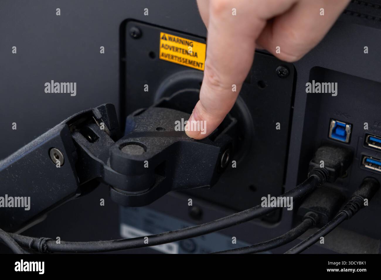 A hand presses a button on a dusty black monitor arm on a computer ...