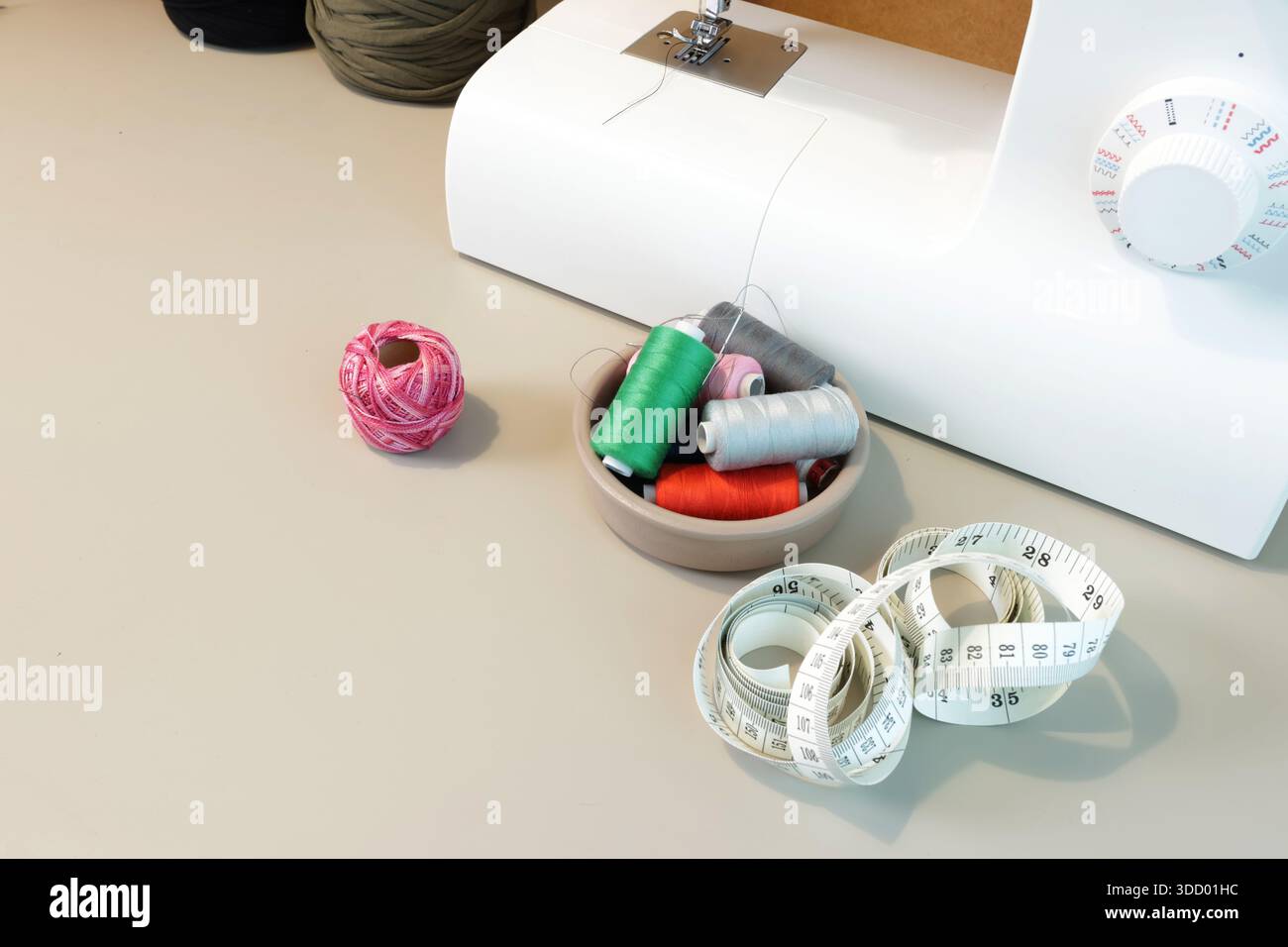 Sewing supplies including colorful thread spools, scissors, and a tape measure on a workbench Stock Photo