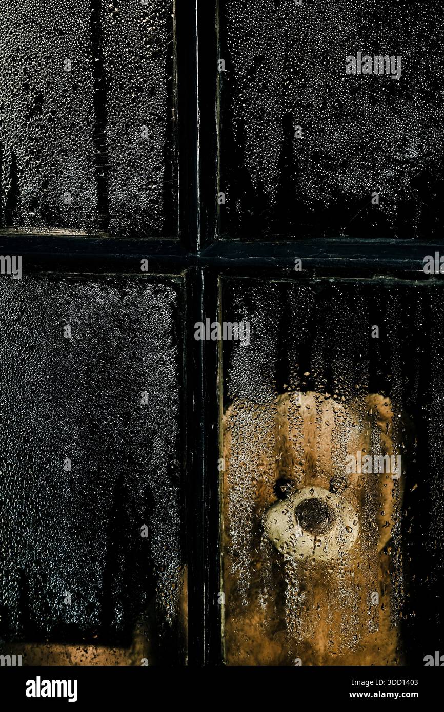 Teddy bear behind window covered in droplets Stock Photo