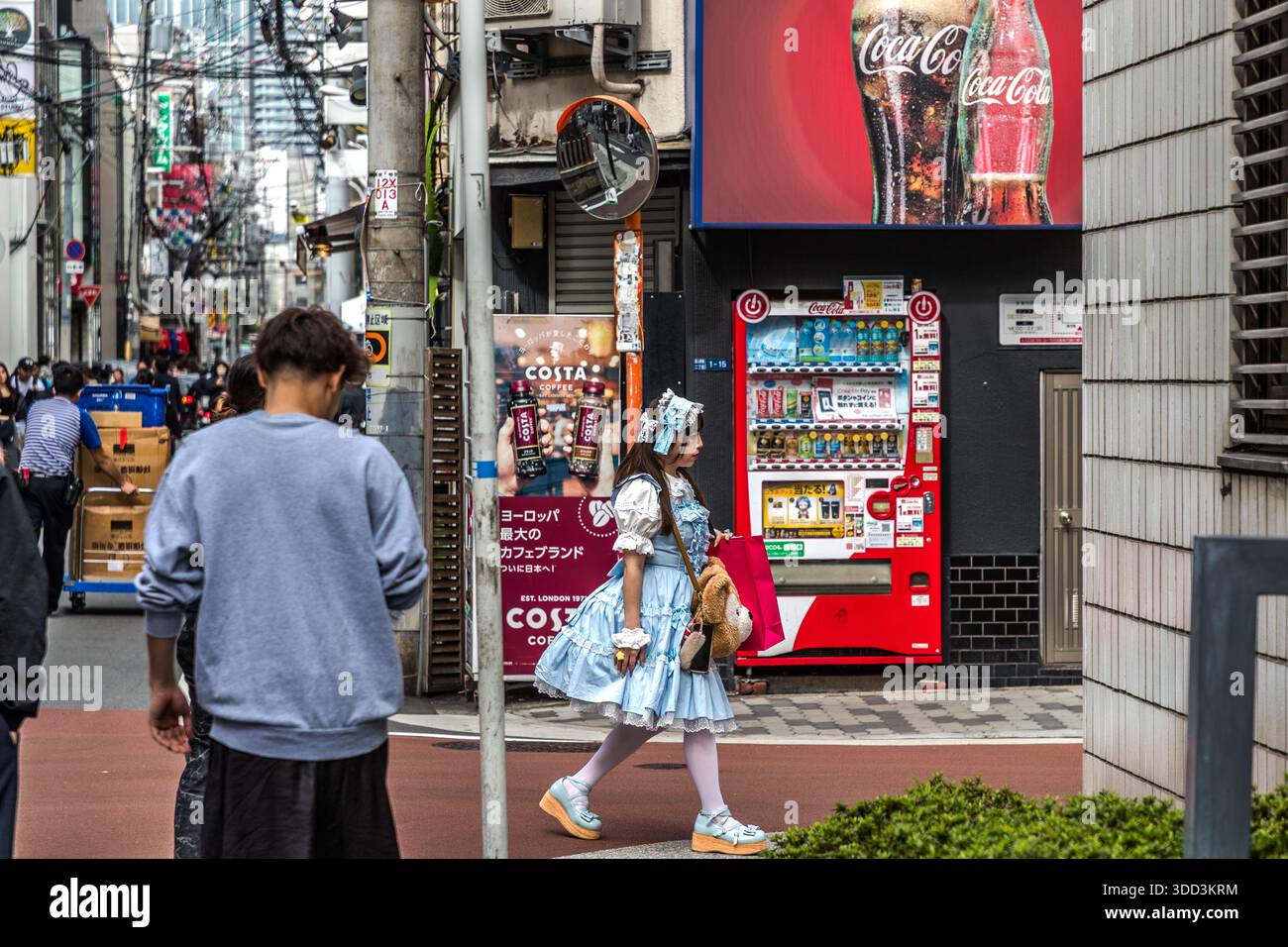 Young woman in Osaka wearing a stylish dirndl outfit with a large handbag in the shape of a teddy bear. Beverage vending machines in the background. Osaka Prefecture, Japan Stock Photo