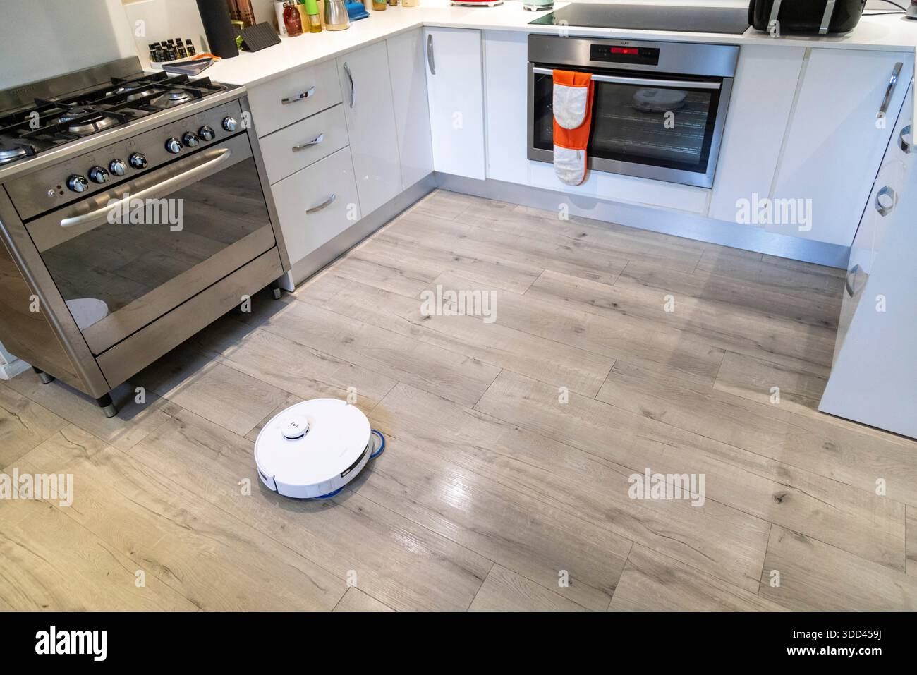 Robotic vacuum cleaner cleaning a wooden kitchen floor Stock Photo