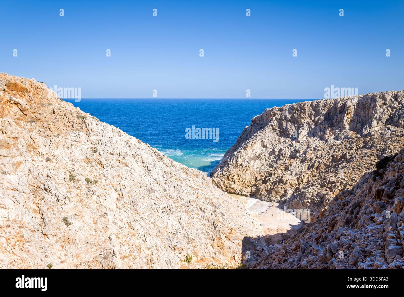 Sun-bleached rocky cliffs form a dramatic gorge leading down to a small ...