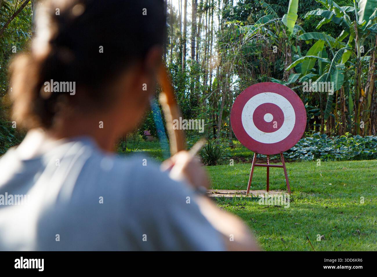 An archer shooting an arrow with a bow at a red wooden bullseye target - Stock Image