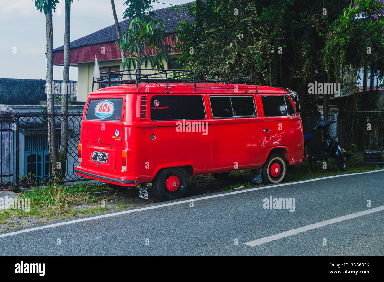 Balikpapan, Indonesia - November 8, 2025. A bright, striking red classic Volkswagen T2 Kombi van, featuring a roof rack and whitewall tires, parked on Stock Photo