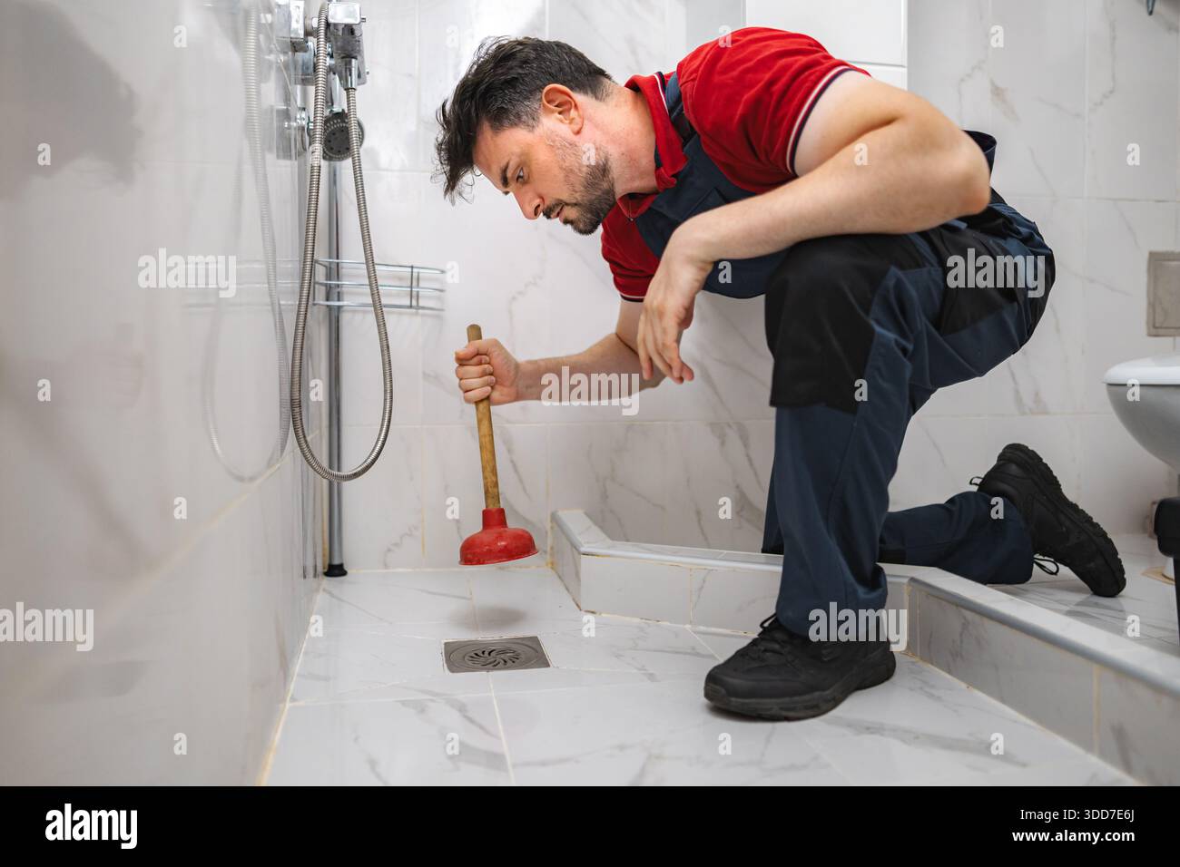 Plumber Using Plunger unclogging shower drain in bathroom Stock Photo