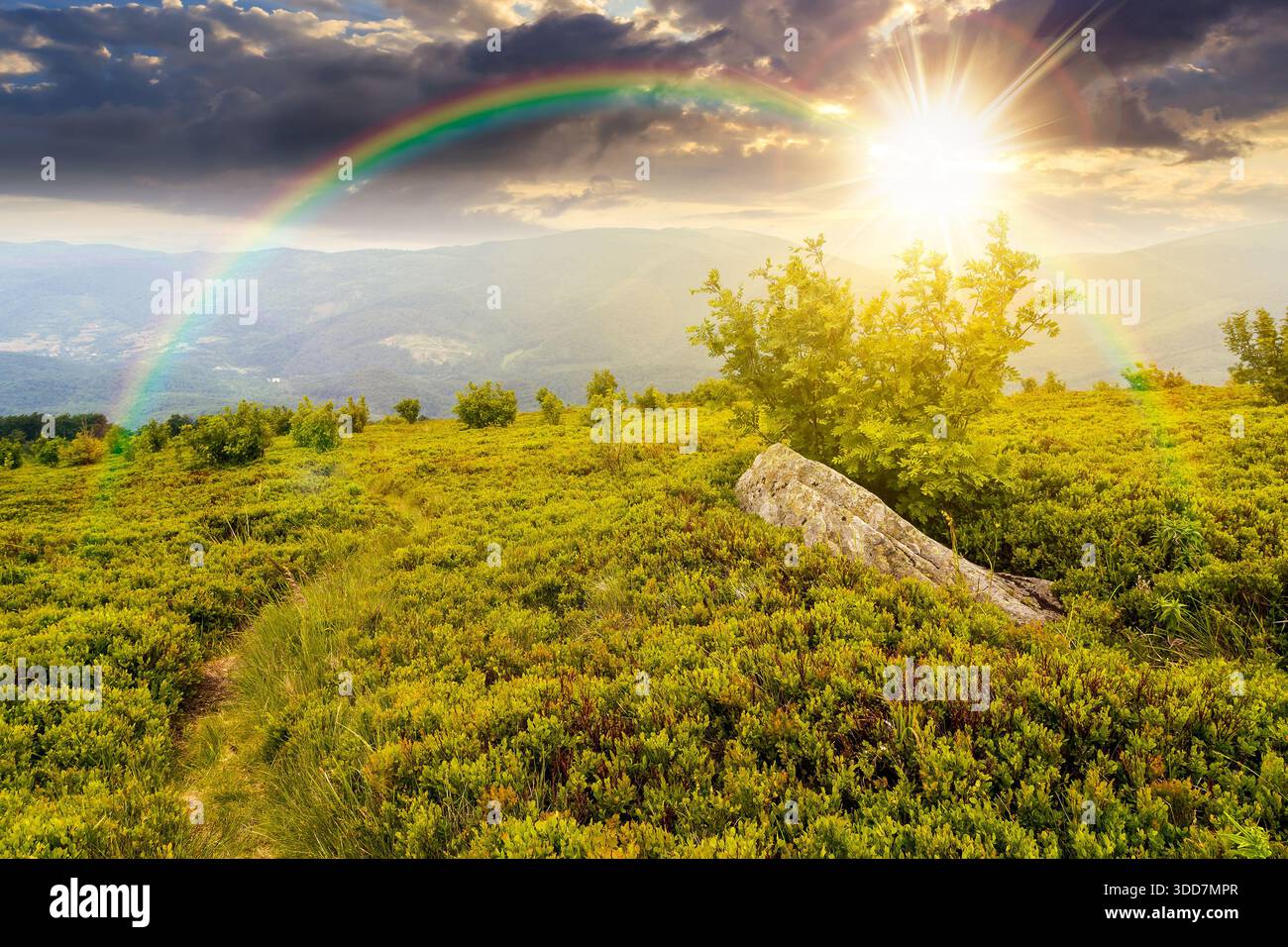 hiking trail through mountain landscape at sunset. mountain range under sky with clouds in evening light. scenery with green grass and rolling hills. Stock Photo