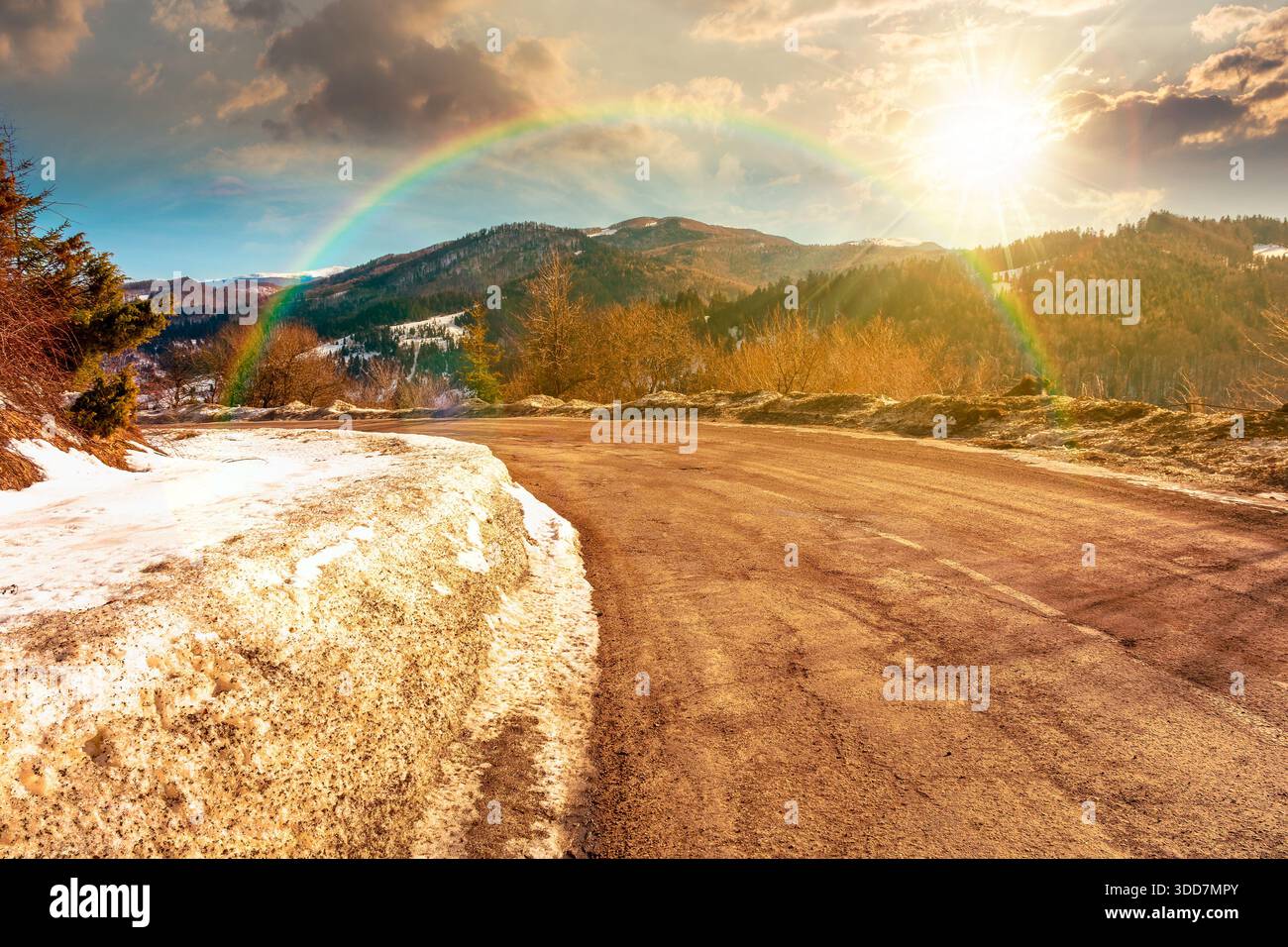 country road winding through winter landscape under blue sky at sunset. mountains in evening light. travel background with snow covered slopes. storyt Stock Photo