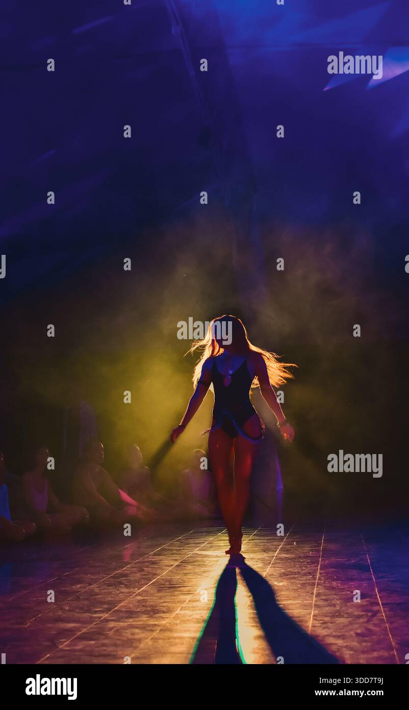 Female performer dancing in colorful stage lighting with fog creating a dramatic atmosphere Stock Photo