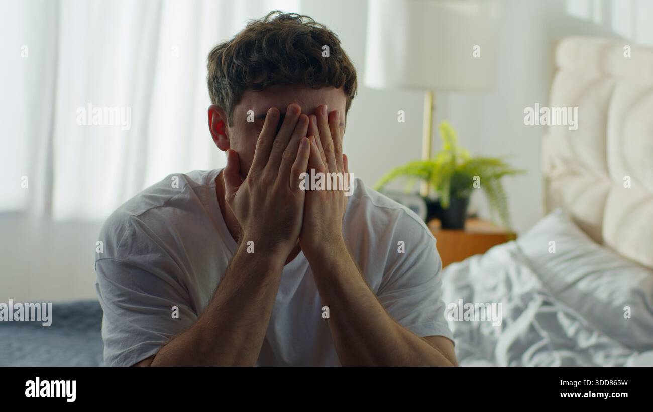 Despairing Caucasian man sitting on bed at home holding head in bedroom European male guy hopeless difficulties crisis grief anxiety distraught Stock Photo