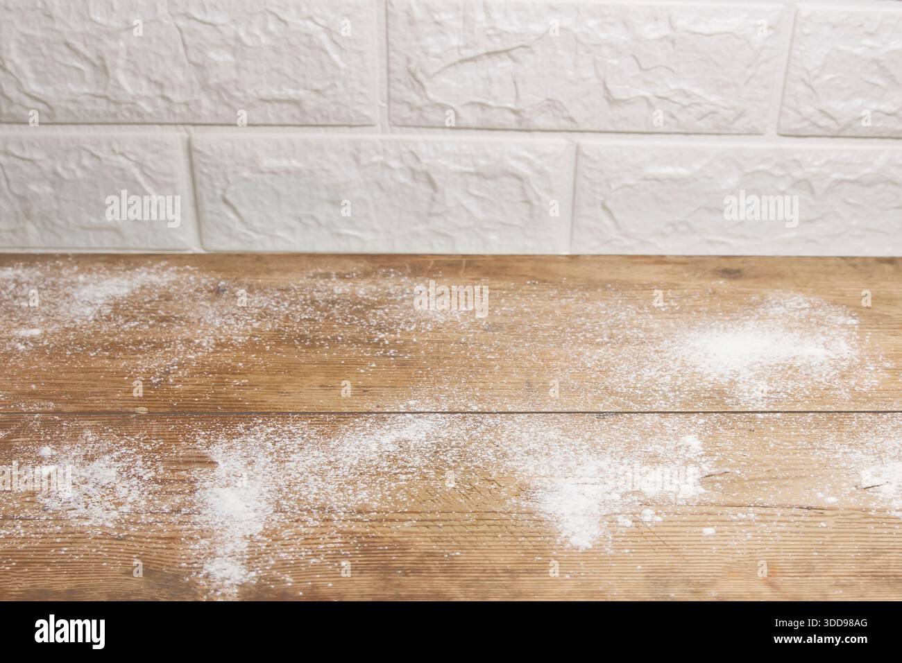 Wooden kitchen table with scattered flour against white brick wall Stock Photo