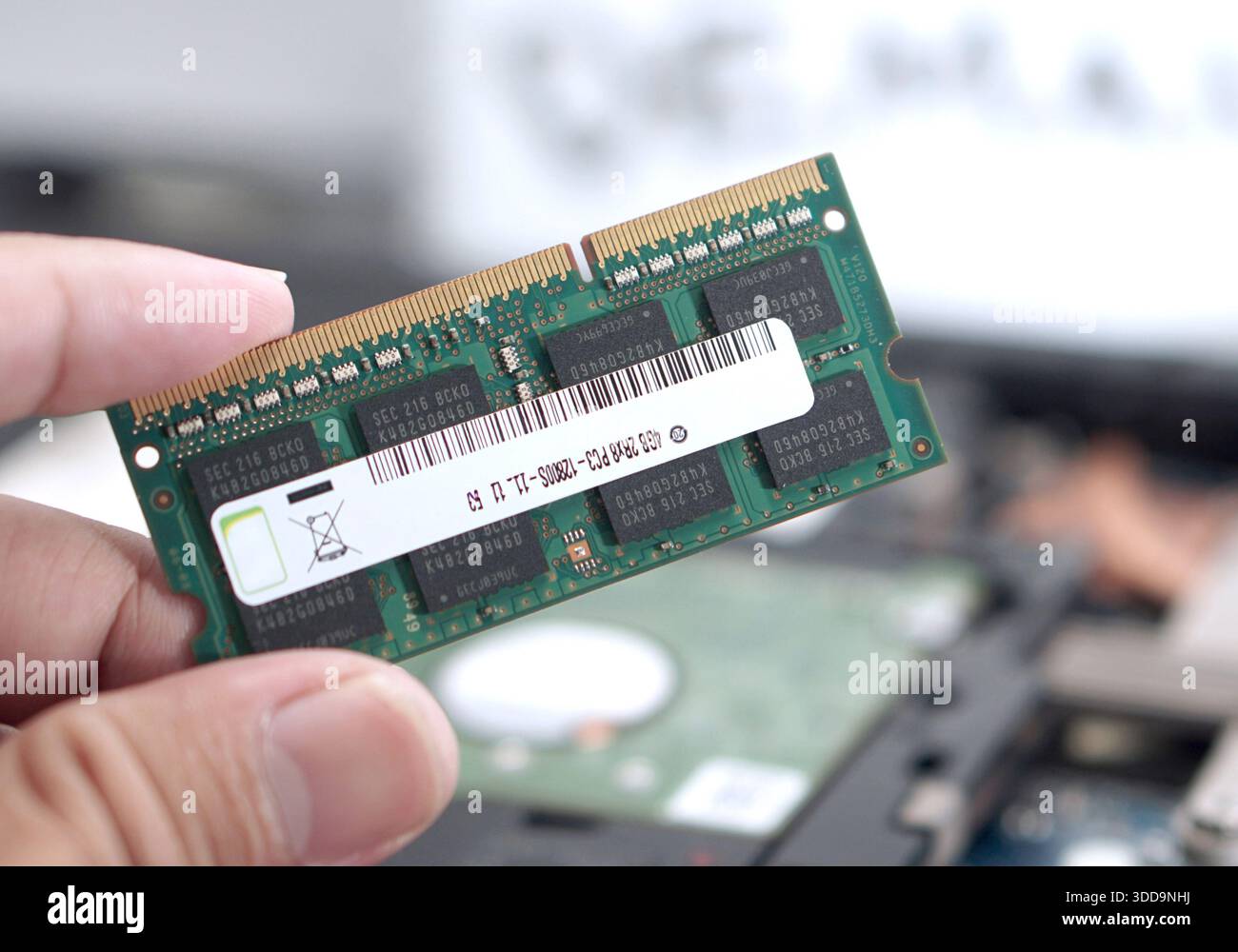 Close-up of fingers holding a green PCB RAM stick against a blurred workshop background. Visual for computer technicians, hardware inspection, and par Stock Photo