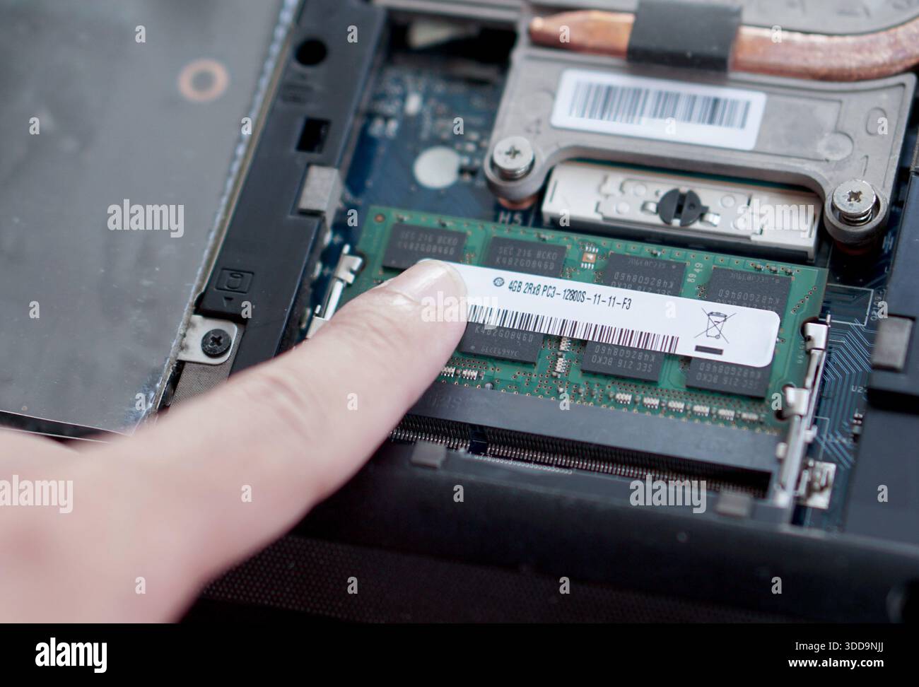 A finger pointing at the specification label of a DDR3 RAM module installed in a laptop. Verifying hardware details and compatibility. Stock Photo