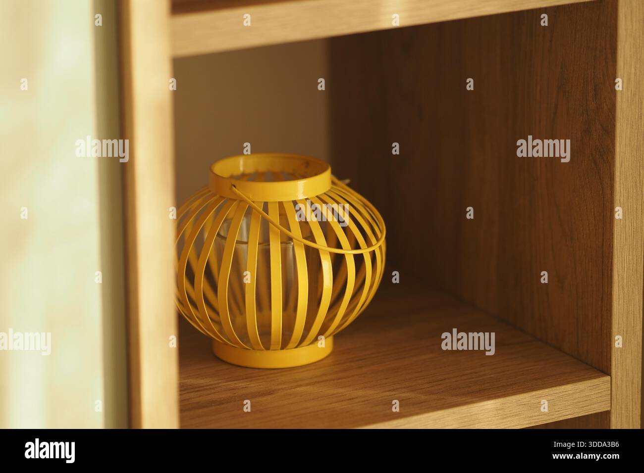 Yellow lantern sits on wooden shelf in bright room Stock Photo