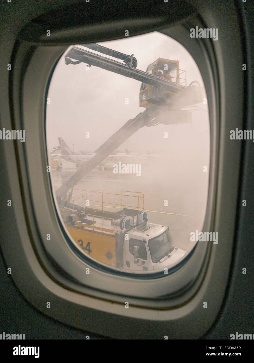 ground crew deicing truck work on a grounded aircraft, viewed from inside the plane. a misty, snowy canadian airport scene highlighting winter operati Stock Photo