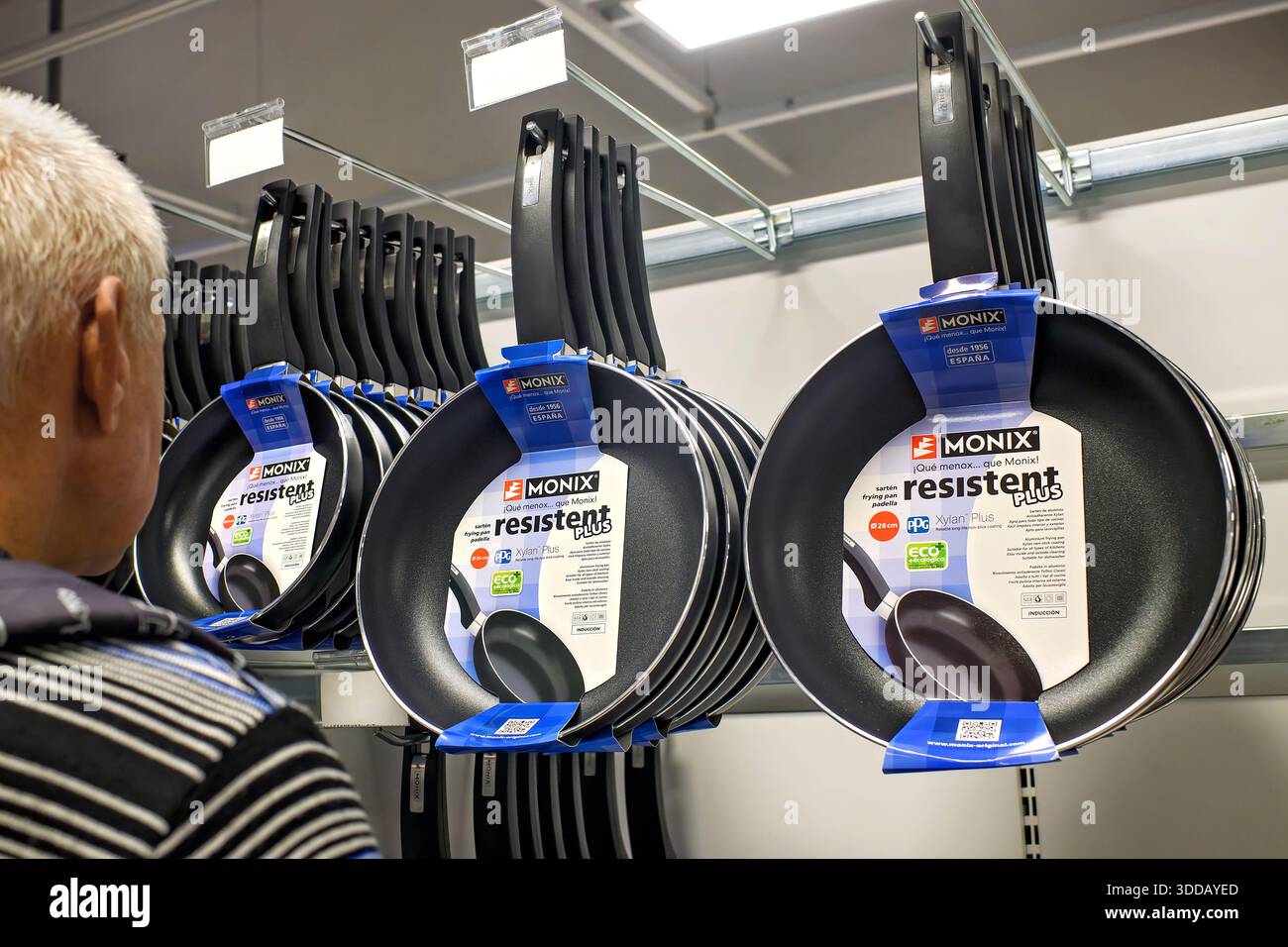 Sliema, Malta - December 24, 2025: A man examines a display of hanging Monix Resistent Plus non-stick frying pans in a store department. Stock Photo