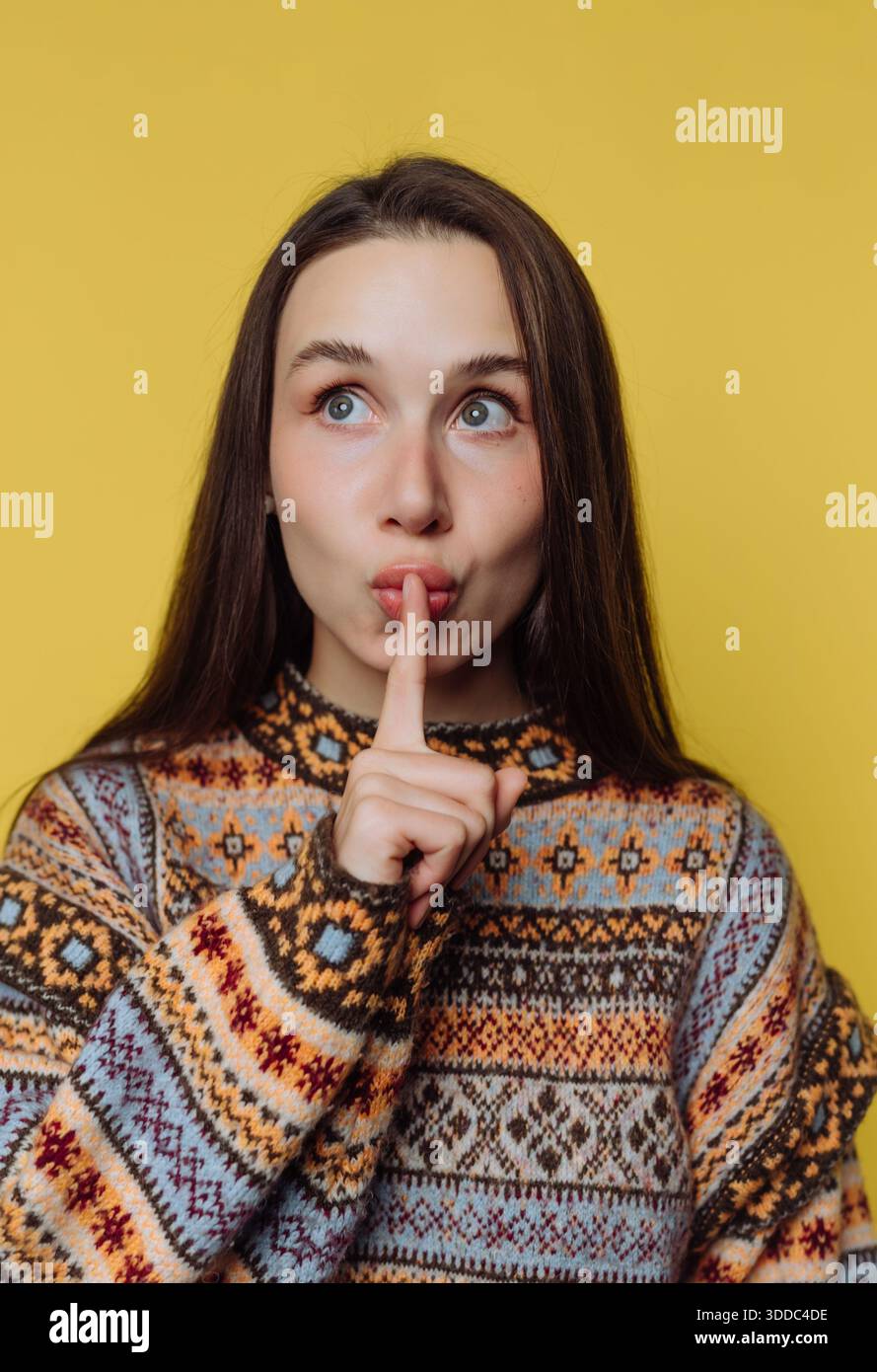 Woman in patterned sweater making a shushing gesture against a yellow background. Stock Photo