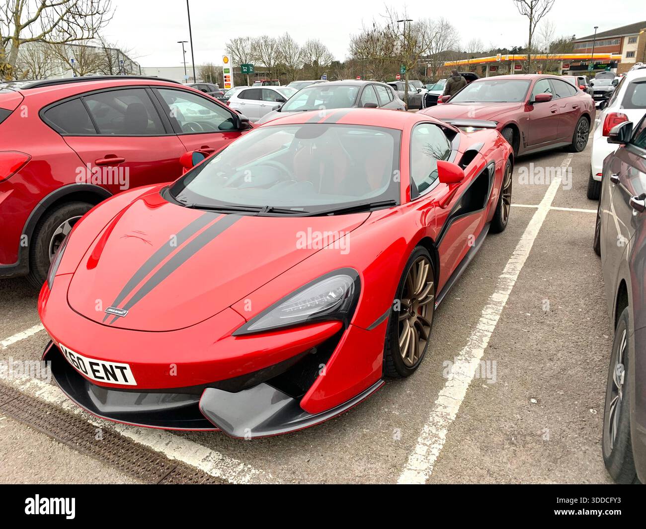 High-performance McLaren sports car with black racing stripes and bronze wheels parked in a public lot surrounded by everyday vehicles urban setting - Smartphone Captured Stock Image