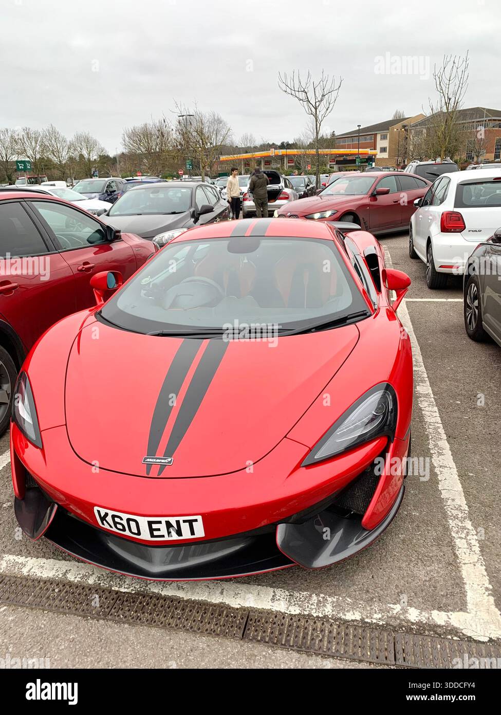 High-performance McLaren sports car with black racing stripes and bronze wheels parked in a public lot surrounded by everyday vehicles urban setting - Smartphone Captured Stock Image