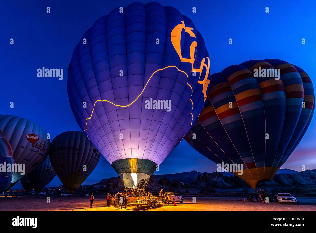 Hot air balloons are inflated near Göreme before sunrise. The baskets can hold up to 32 people and are secured to a trailer before take-off. Central Anatolia Region, Turkey Stock Photo