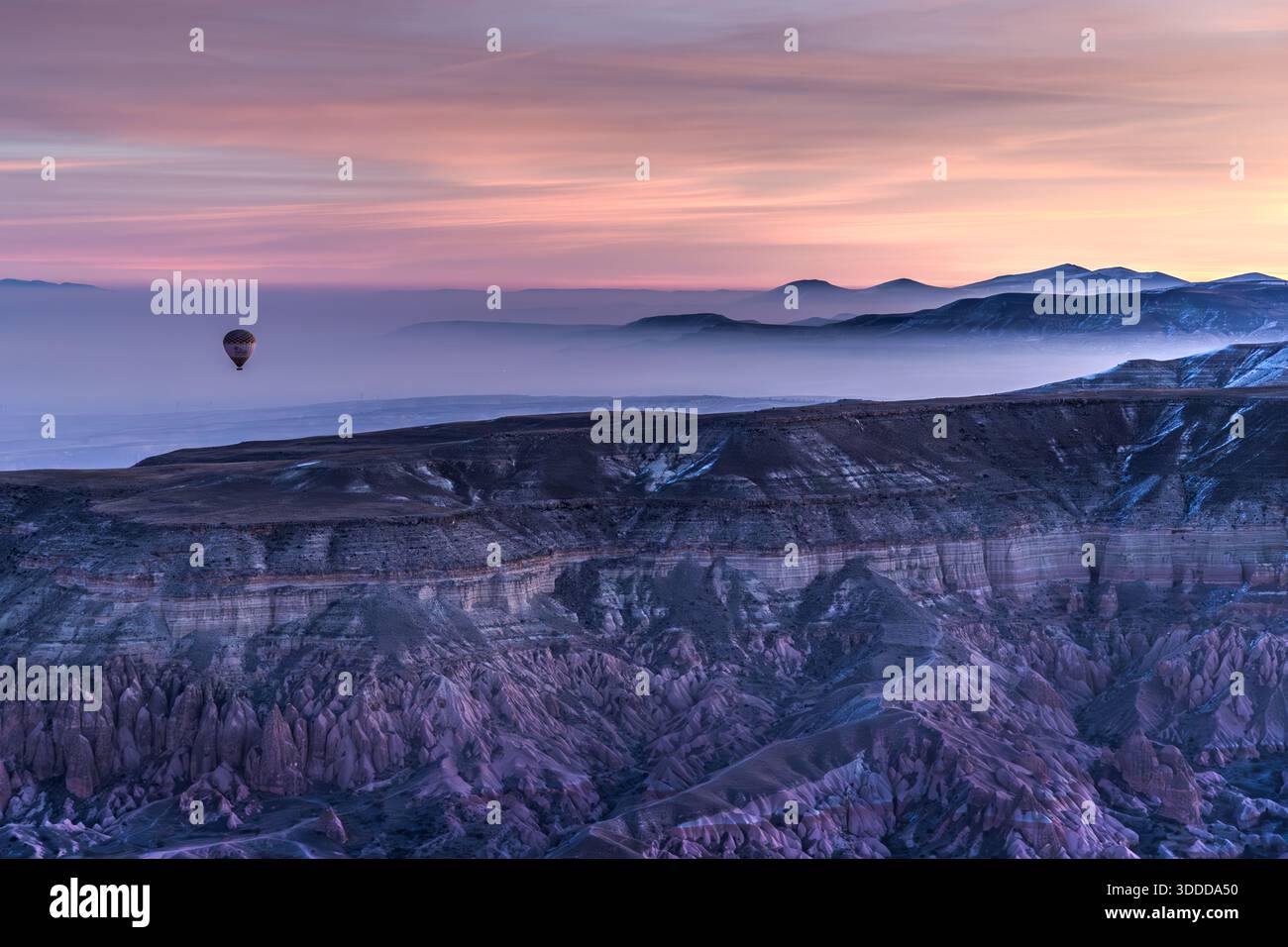 Hot air balloons rise above the rock formations of Göreme at sunrise, Central Anatolia Region, Turkey. Tuff stone landscape and fairy chimneys Stock Photo