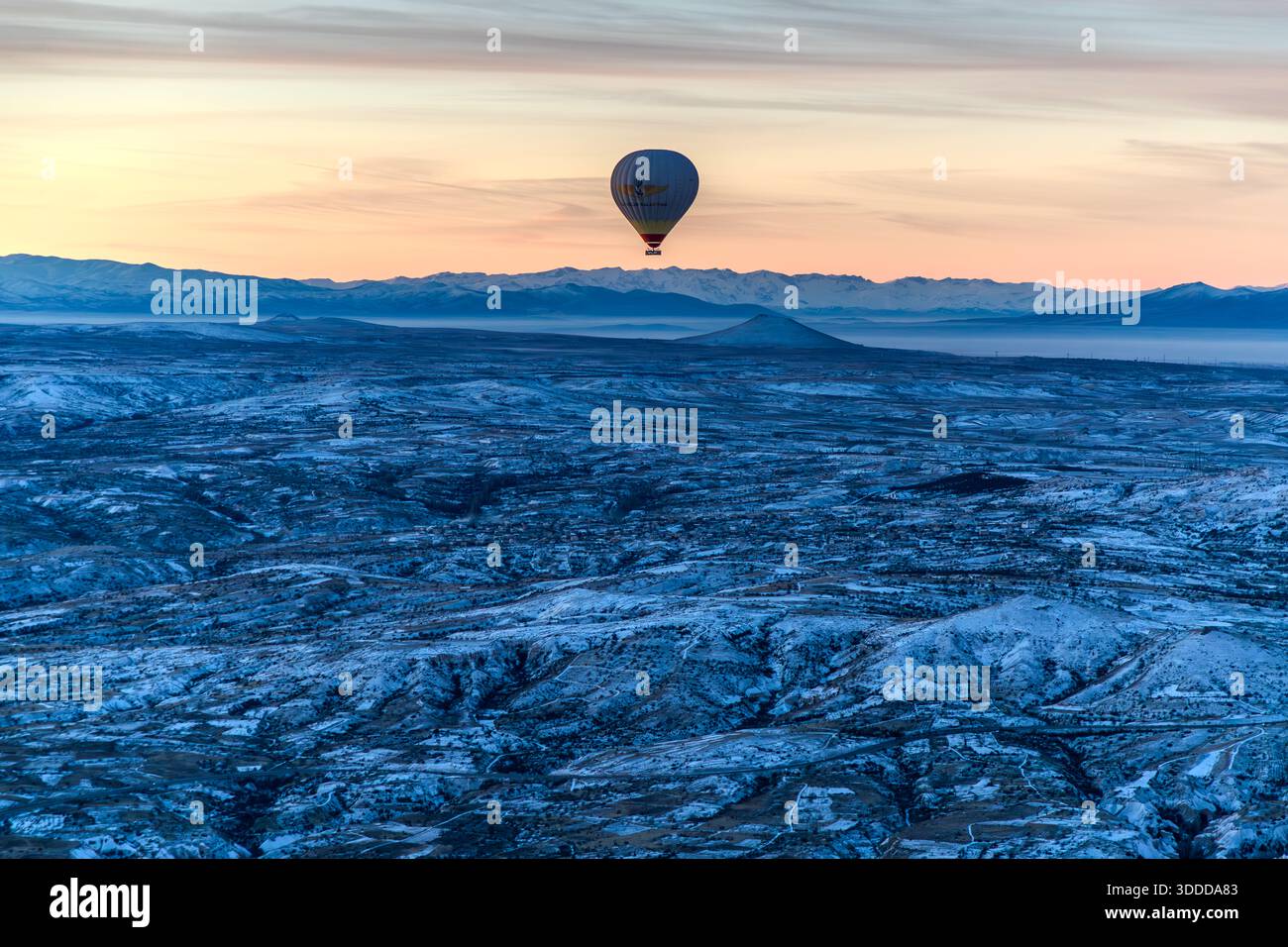 Hot air balloon flies over snow-covered landscape in Göreme, Central Anatolia Region, Turkey Stock Photo