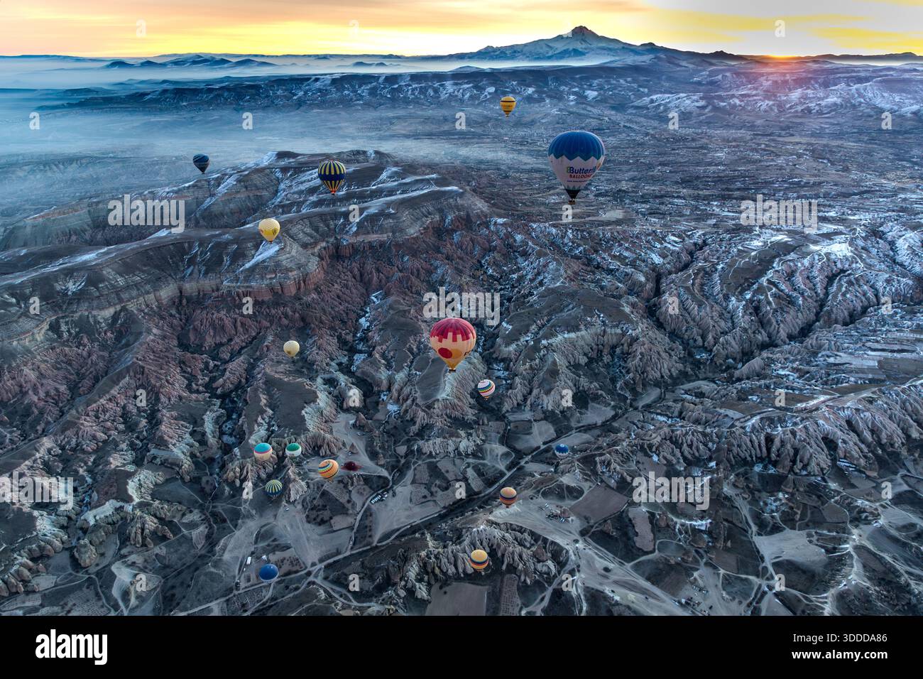 Hot air balloons float over the surreal landscape of Göreme, Turkey, at sunrise with the Erciyes Dağı volcano in the background, Central Anatolia Region, Turkey Stock Photo