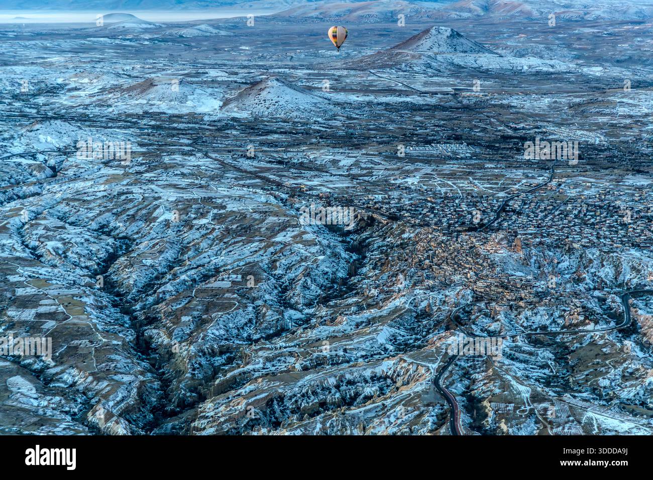 Hot air balloon flies over snow-covered landscape in Göreme, Central Anatolia Region, Turkey Stock Photo