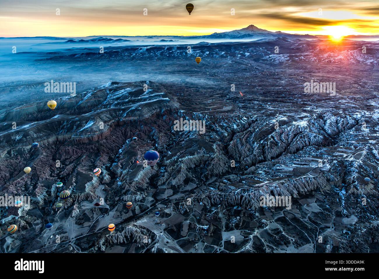 Sunrise with hot air balloons in front of the Erciyes Dağı volcano. Hot air balloons float over the surreal landscape of Göreme, Turkey, at sunrise with the Erciyes Dağı volcano in the background, Central Anatolia Region, Turkey Stock Photo