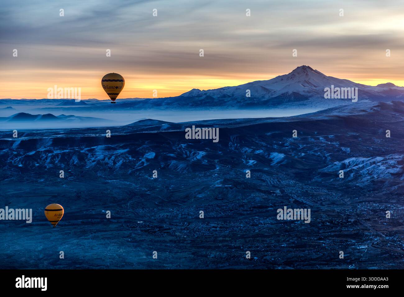 Hot air balloons float over the surreal landscape of Göreme, Turkey, at sunrise with the Erciyes Dağı volcano in the background, Central Anatolia Region, Turkey Stock Photo
