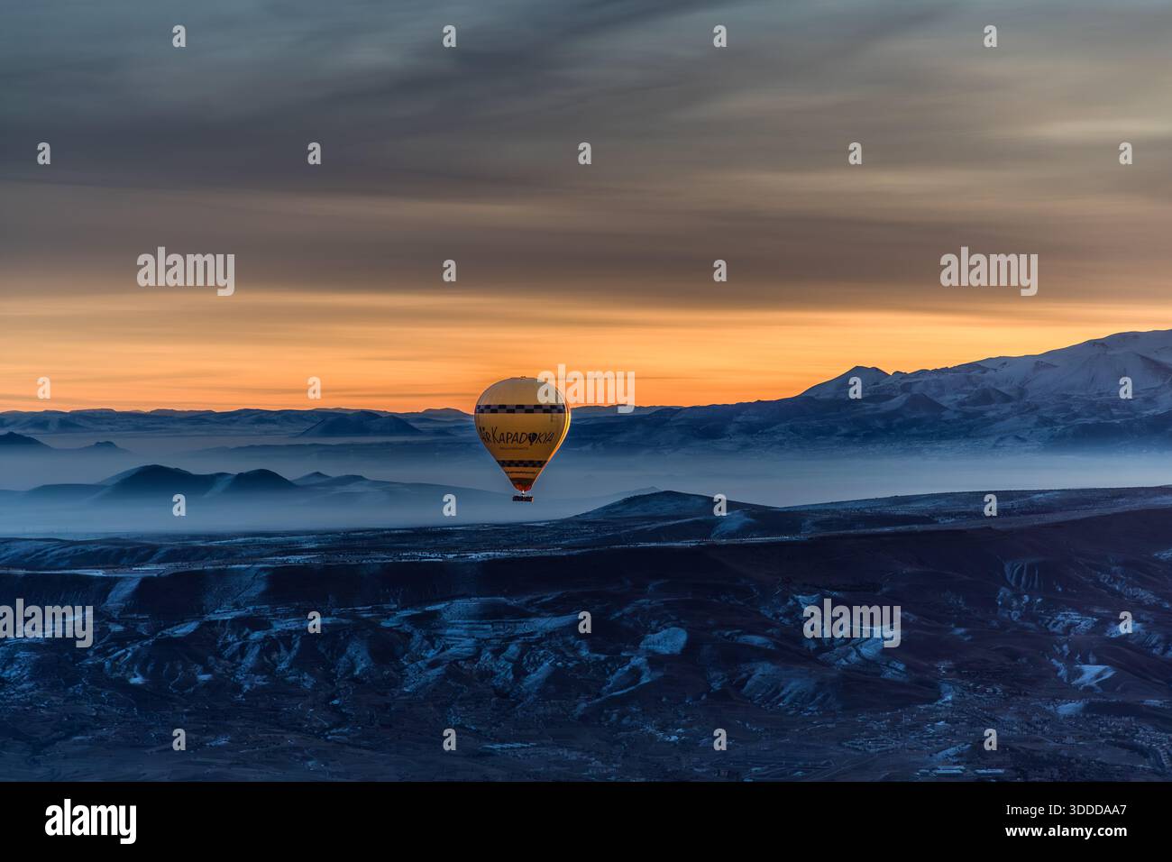 Hot air balloon flies over snow-covered landscape in Göreme, Central Anatolia Region, Turkey Stock Photo