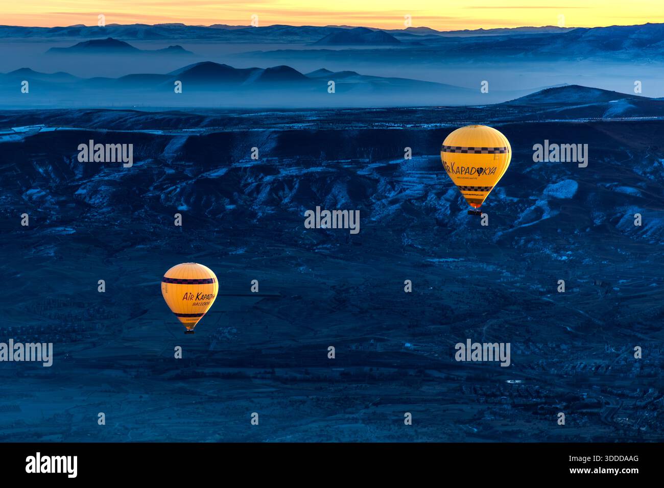 Two hot air balloons float above the snow-covered landscape near Göreme, Cappadocia, before sunrise. Central Anatolia Region, Turkey Stock Photo