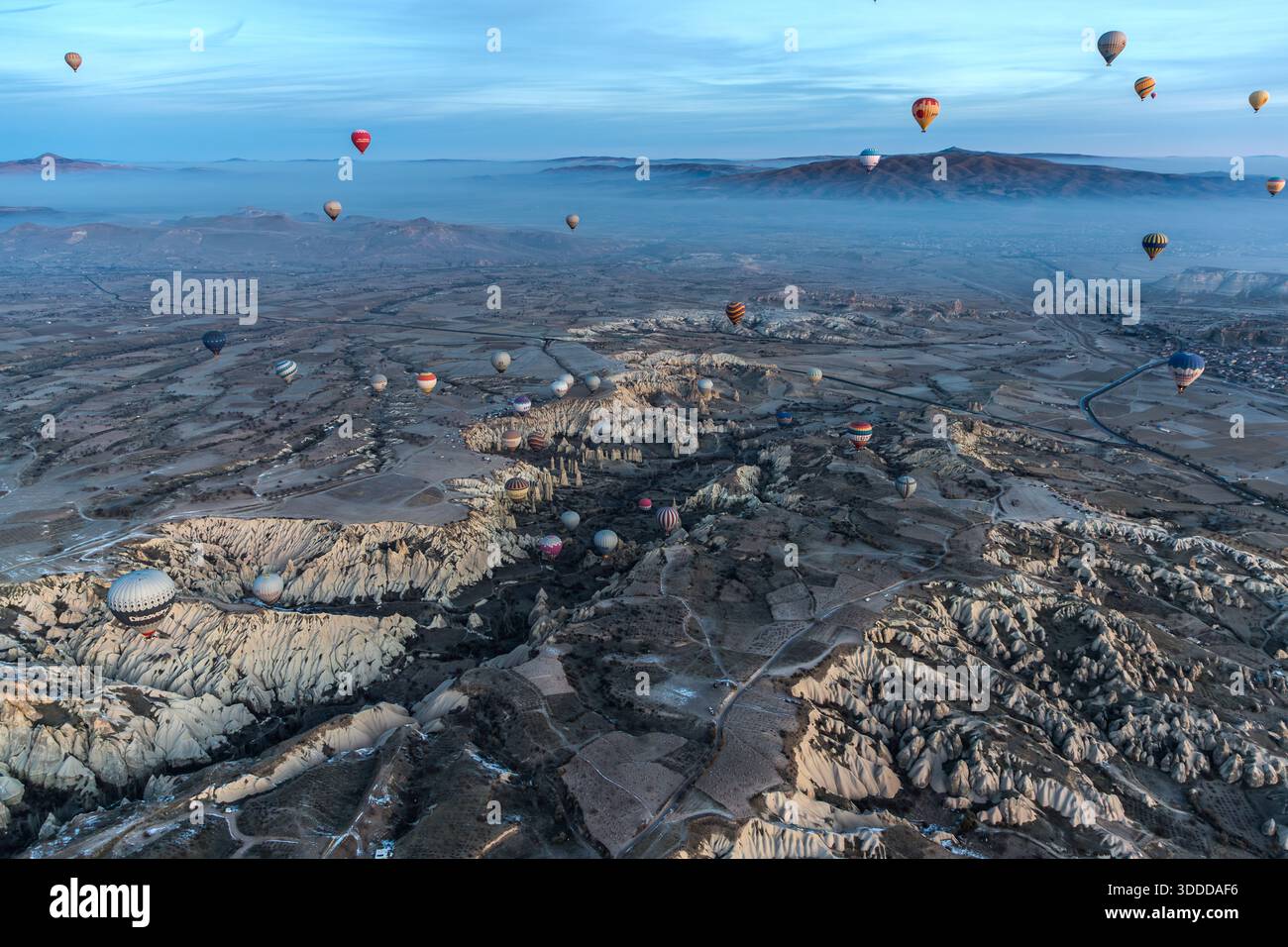 Hot air balloon flies over snow-covered landscape in Göreme, Central Anatolia Region, Turkey. Tuff stone landscape and fairy chimneys Stock Photo