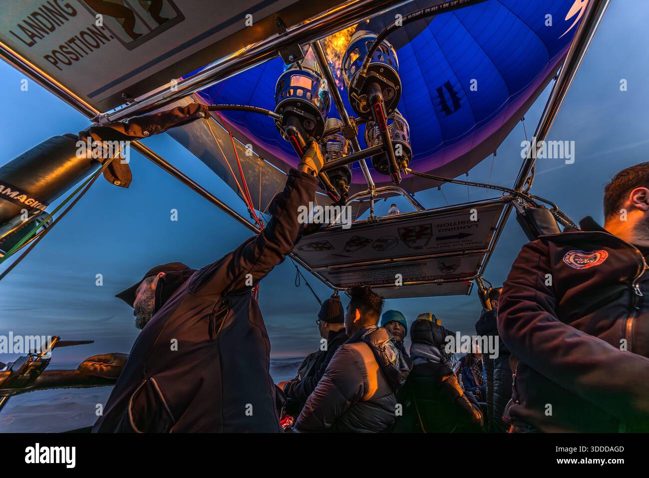 Passengers and pilots on a pre-sunrise balloon ride over Göreme, Cappadocia, Turkey; the pilot ignites the burner. Commercial balloon flights over Cappadocia date back to 1991, founded by British pilot Kaili Kidner and her Swedish husband Lars-Eric Möre; today around 27 licensed companies operate roughly 250 balloons, with up to 156 flights and 3,000 to 4,000 passengers a day. Stock Photo