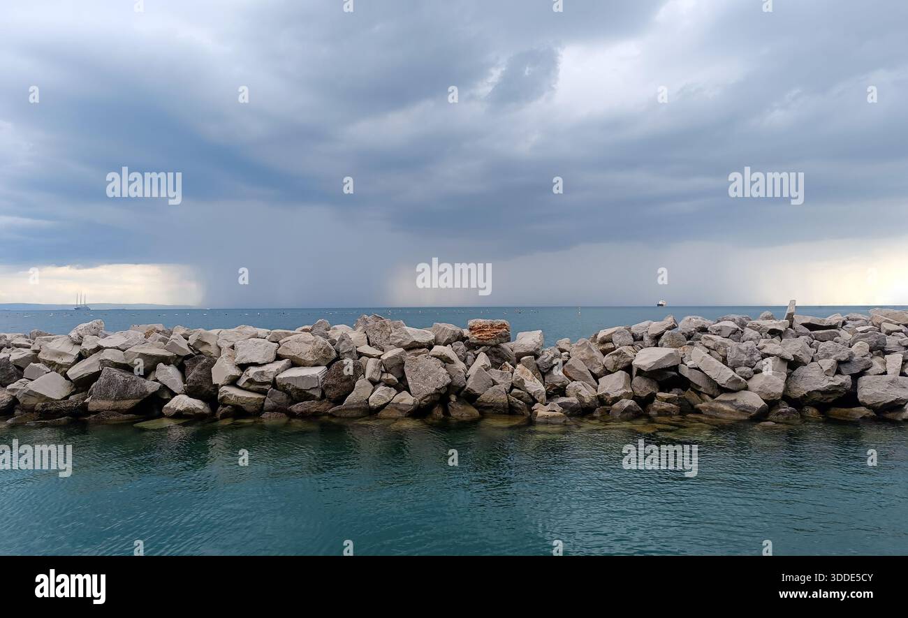 Storm clouds and rain over the sea behind rocky breakwater Stock Photo