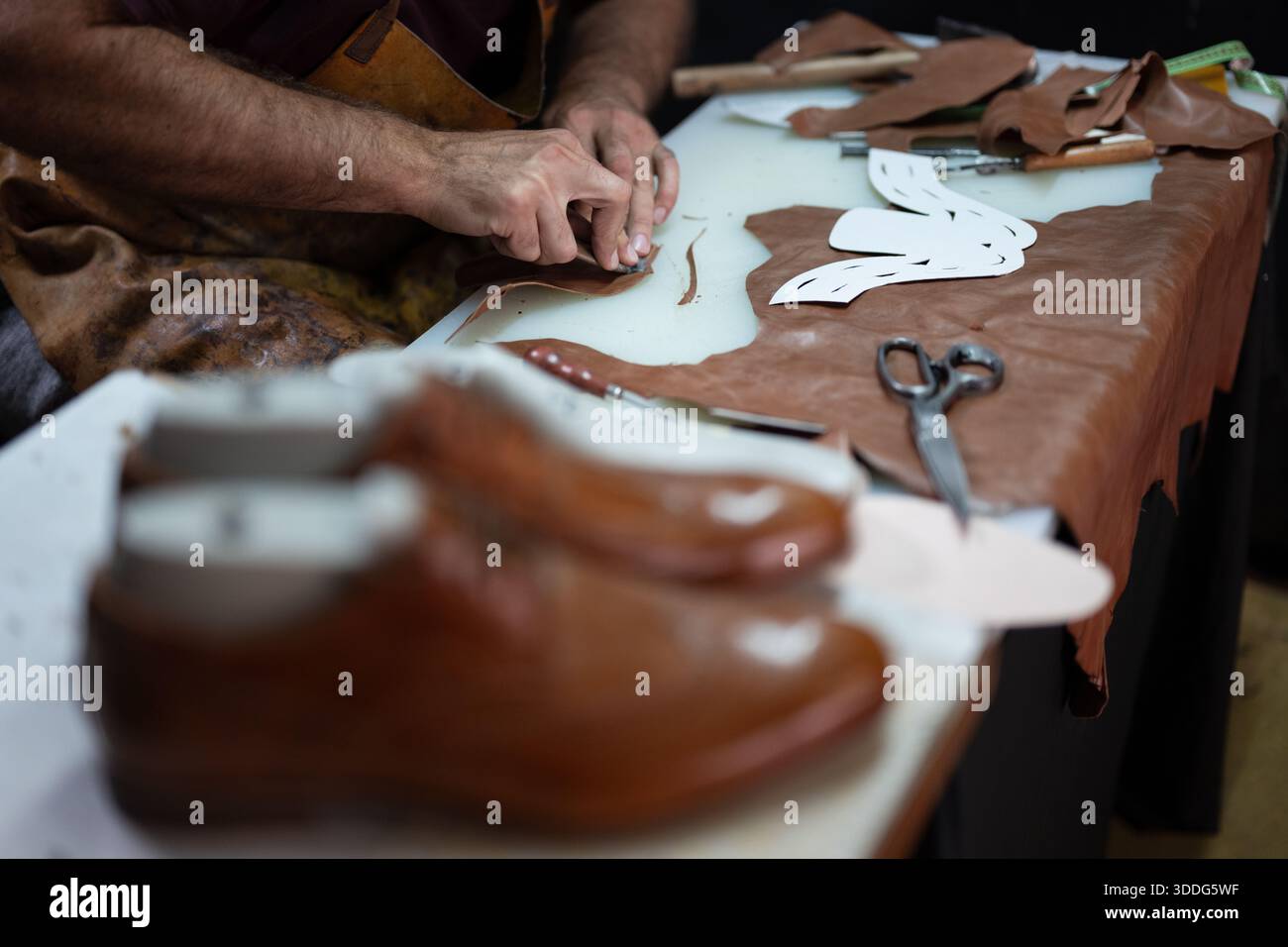 Leather craftsman at work shaping leather with tools and patterns on a workshop table Stock Photo