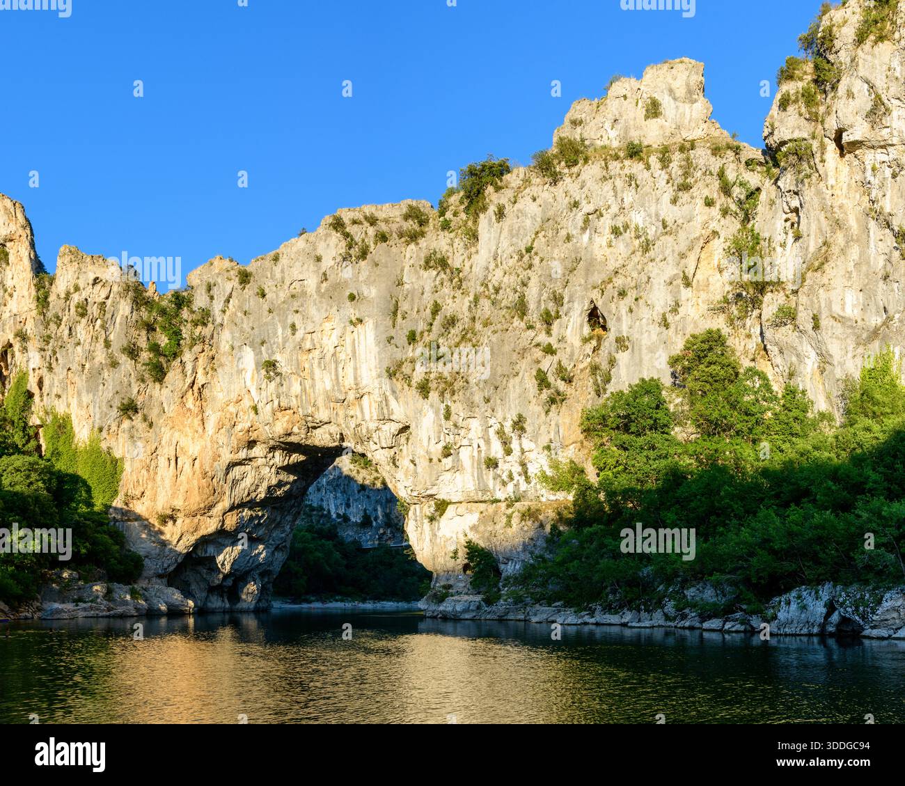 The iconic Pont d'Arc limestone arch rises above a calm river, its ...