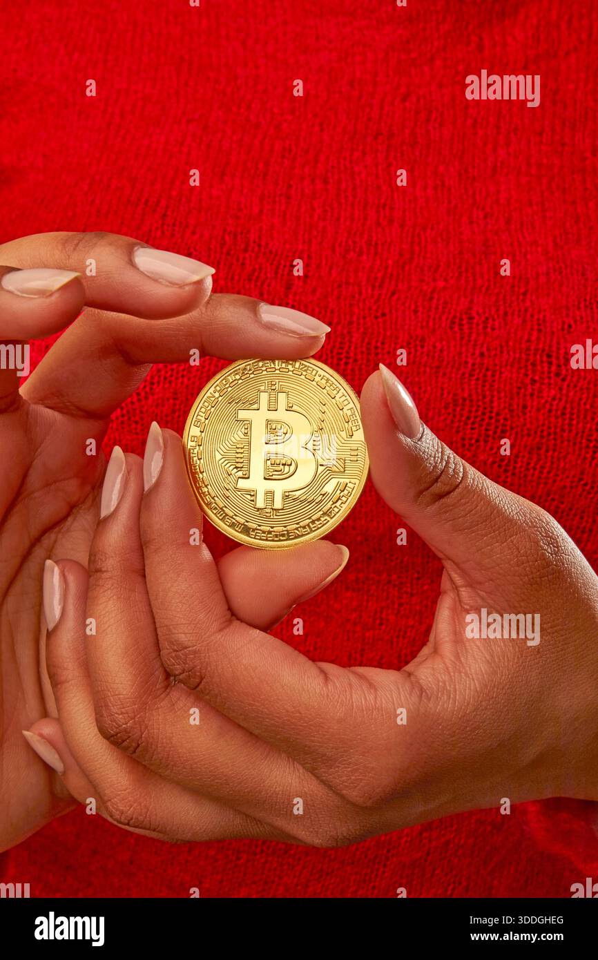 A person is holding a round coin with the Bitcoin logo in their hands. The  setting is casual, and the person appears focused on the coin Stock Photo -  Alamy