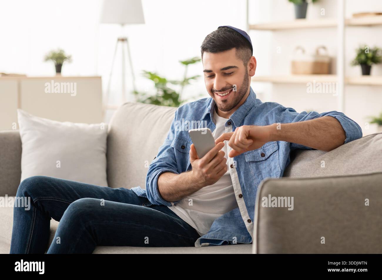 Smiling jew man using smart phone sitting on couch Stock Photo