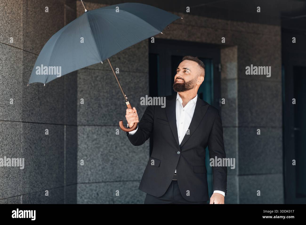 Mature office worker wearing classical suit holding umbrella while walking outdoors, going home after work in office Stock Photo
