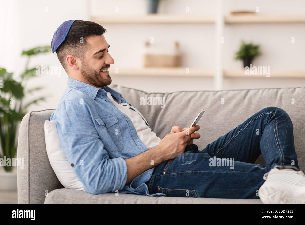 Smiling jew man using mobile phone sitting on couch Stock Photo