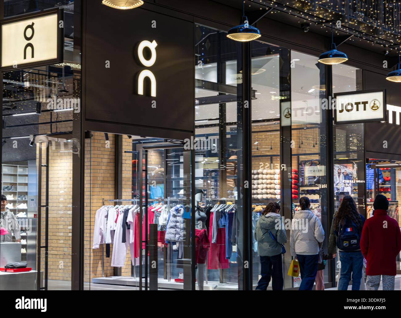 People looking into a brightly lit Jott and Qn apparel store at in the ...