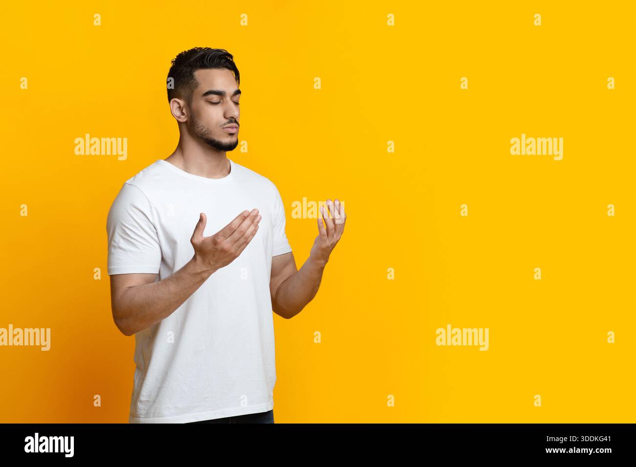 Religious young arab man praying on yellow background, copy space Stock Photo
