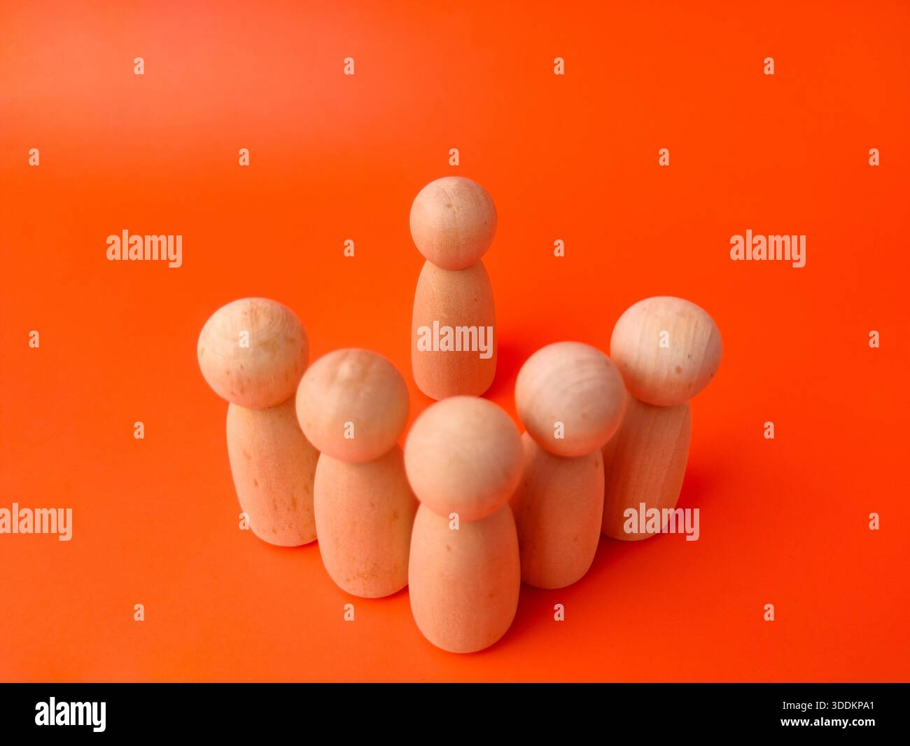 Six wooden peg dolls on an orange background. These types of photos are commonly used as visual metaphors in various contexts, particularly in busines Stock Photo