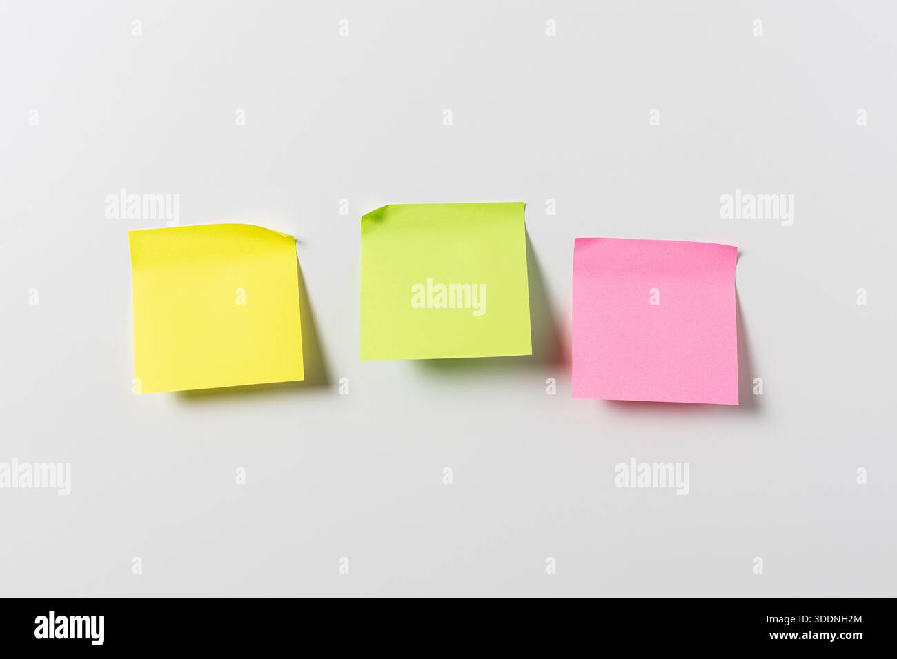 Three blank colorful sticky notes on white wall. Template mock up Stock Photo