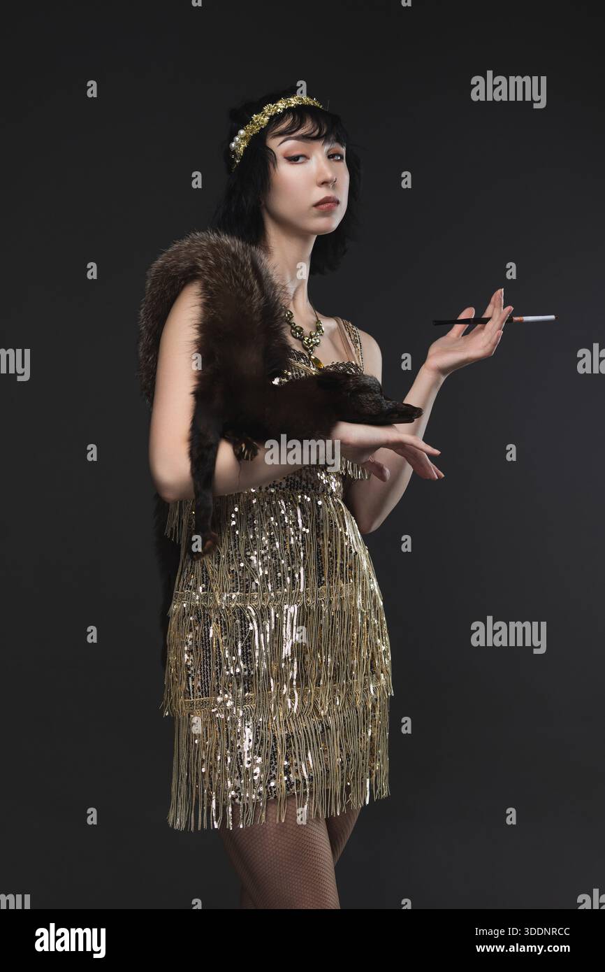 1920s femme fatale in gold Art Deco dress with beaded headband, brunette bob. Stock Photo