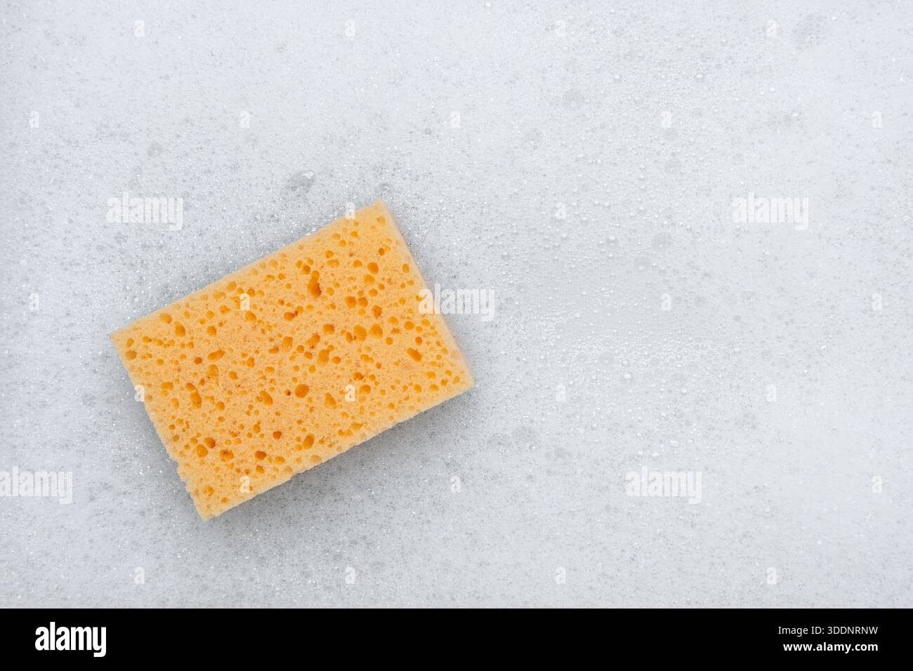 Yellow sponge on a white soapy foam background. Top view.м Stock Photo