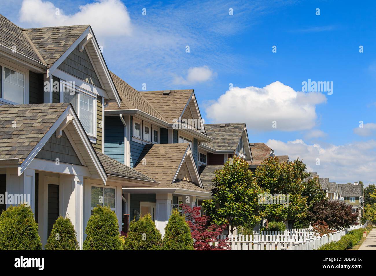 Modern houses line the street under a blue sky with clouds Stock Photo ...