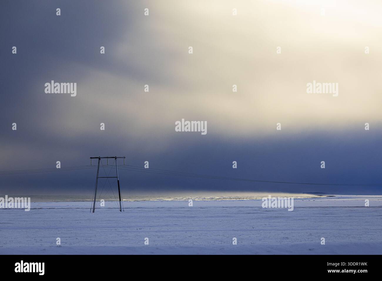 View of stark, snow-covered plains stretch under a dramatic sky, where dark, brooding clouds meet a soft, ethereal glow on horizon, Golden Circle, Ice Stock Photo