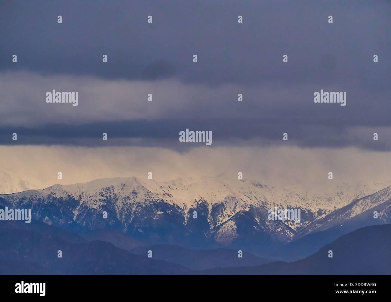 Snow-Covered Mountain Range Under Heavy Dark Clouds at Dusk, Serene Winter Landscape Stock Photo